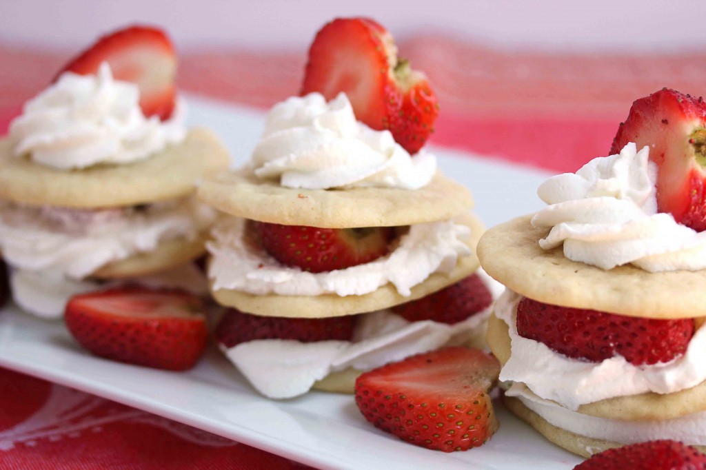 Three strawberry shortcake tea cake stacks served on a square, white plate with sliced strawberries between each one