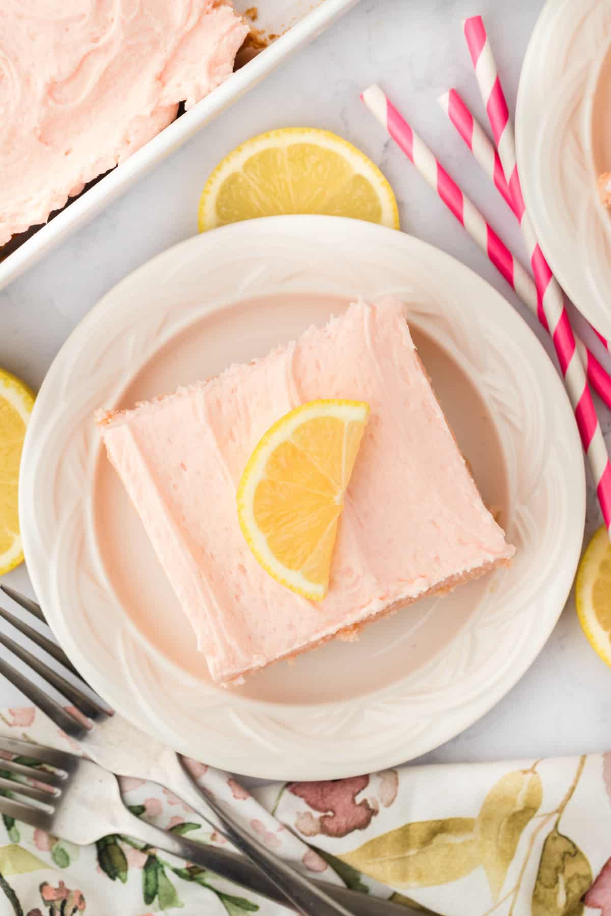 a square slice of pink lemonade cake topped with a lemon.
