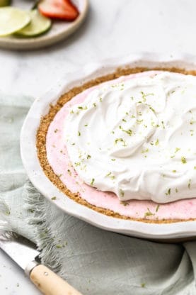 A frozen strawberry pie with whipped cream and lime zest in pie plate under a towel