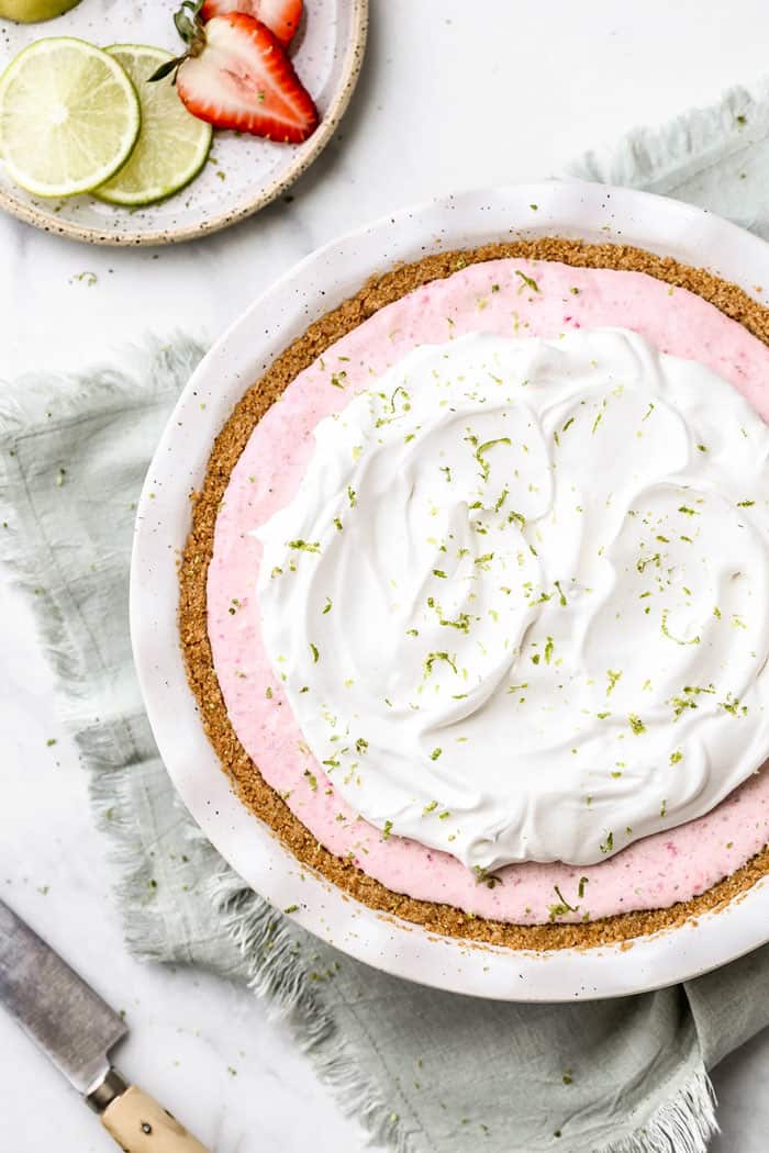 Overhead of Strawberry Margarita Pie in pie plate with slices of limes and strawberries on the side