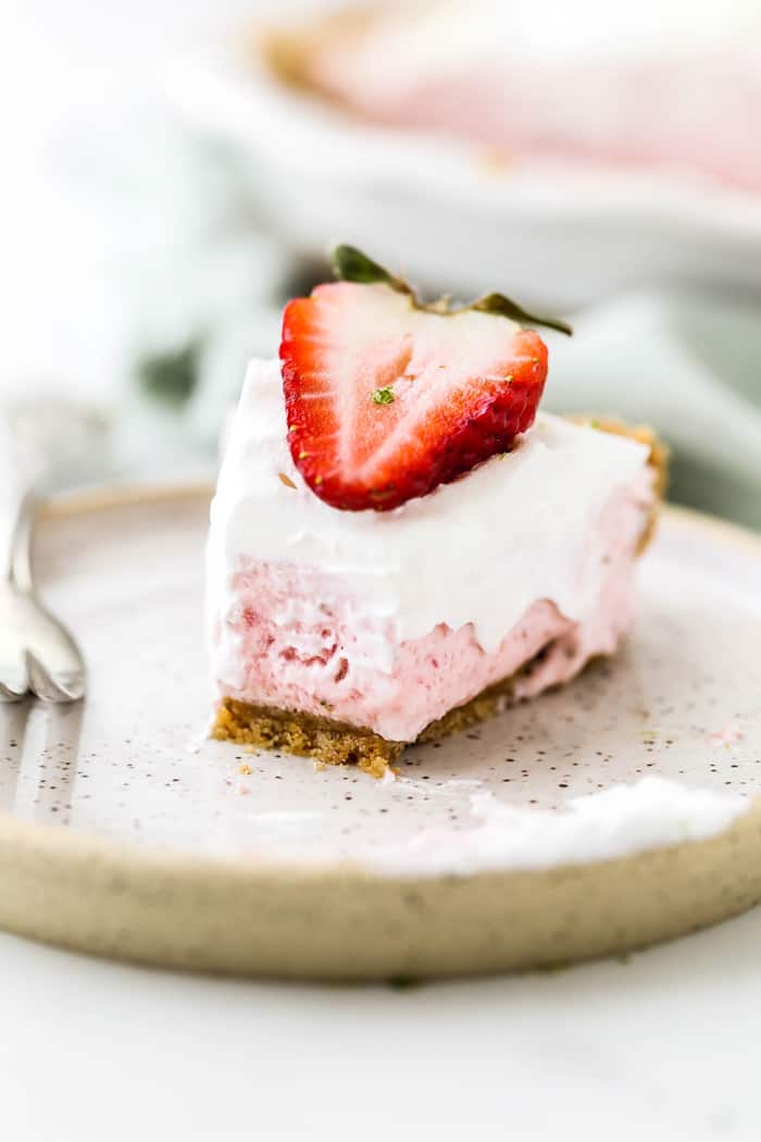 A slice of Strawberry Pie half eaten with a strawberry slice on top and fork nearby