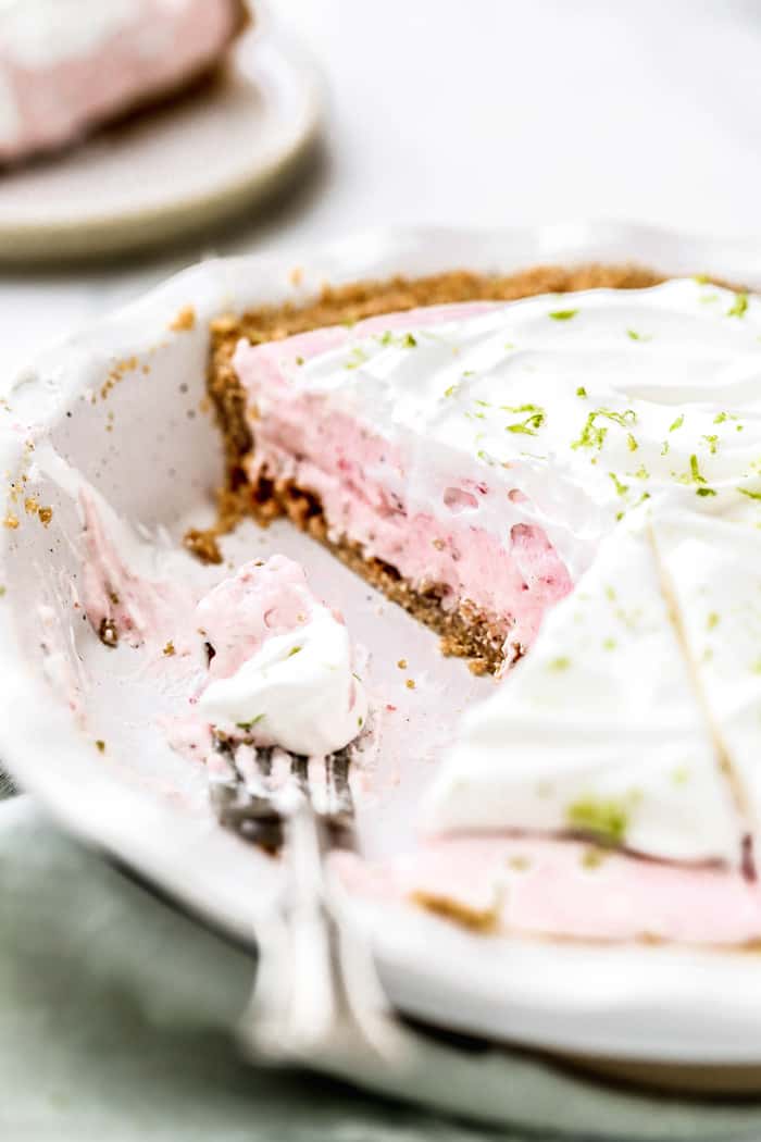 Slices missing from Strawberry Margarita Pie in pie plate with pie filling on fork in plate