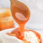 Vanilla ice cream in a white bowl with a spoon in it topped with caramel sauce.