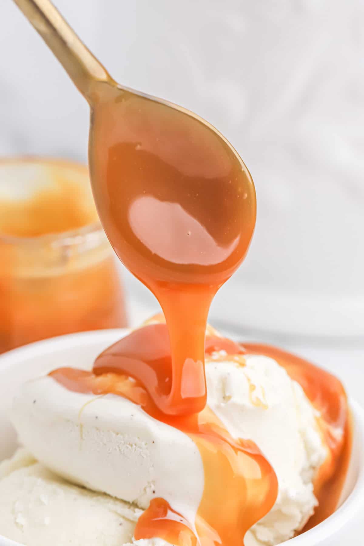 A spoon drizzling some caramel sauce over the top of ice cream.