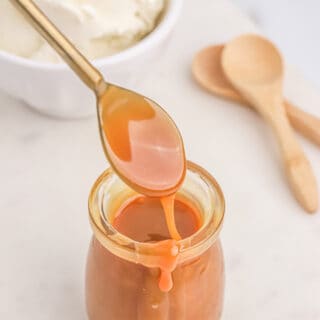 A jar of homemade caramel sauce on the counter with a spoon dipping into it.