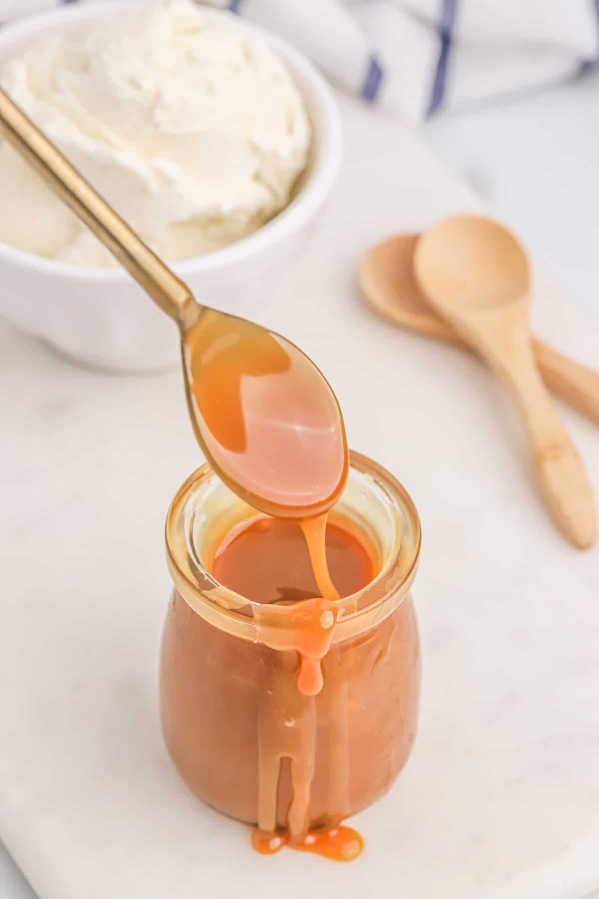 A jar of homemade caramel sauce on the counter with a spoon dipping into it.