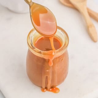 A jar of homemade caramel sauce with a spoonful held up over the jar.