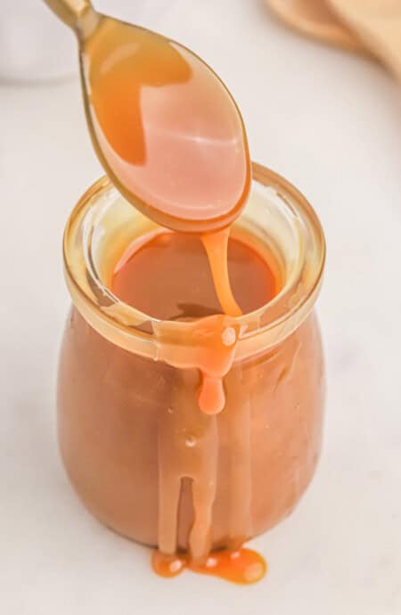 A jar of homemade caramel sauce with a spoonful held up over the jar.