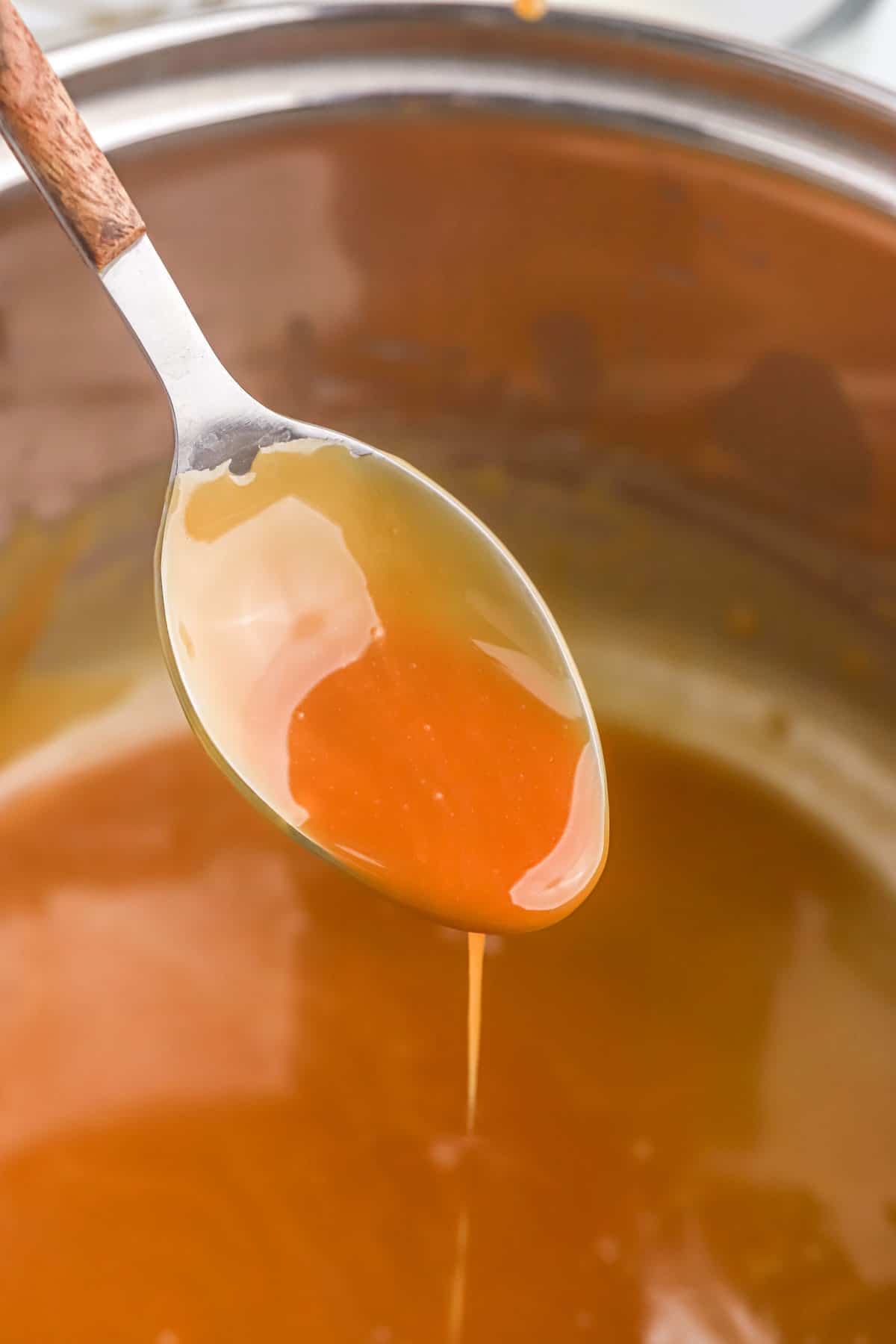 A spoon with caramel sauce dripping back into the pot.
