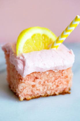 Close up of a square piece of Pink Lemonade Cake topped with a lemon wedge and a yellow and white striped straw in it