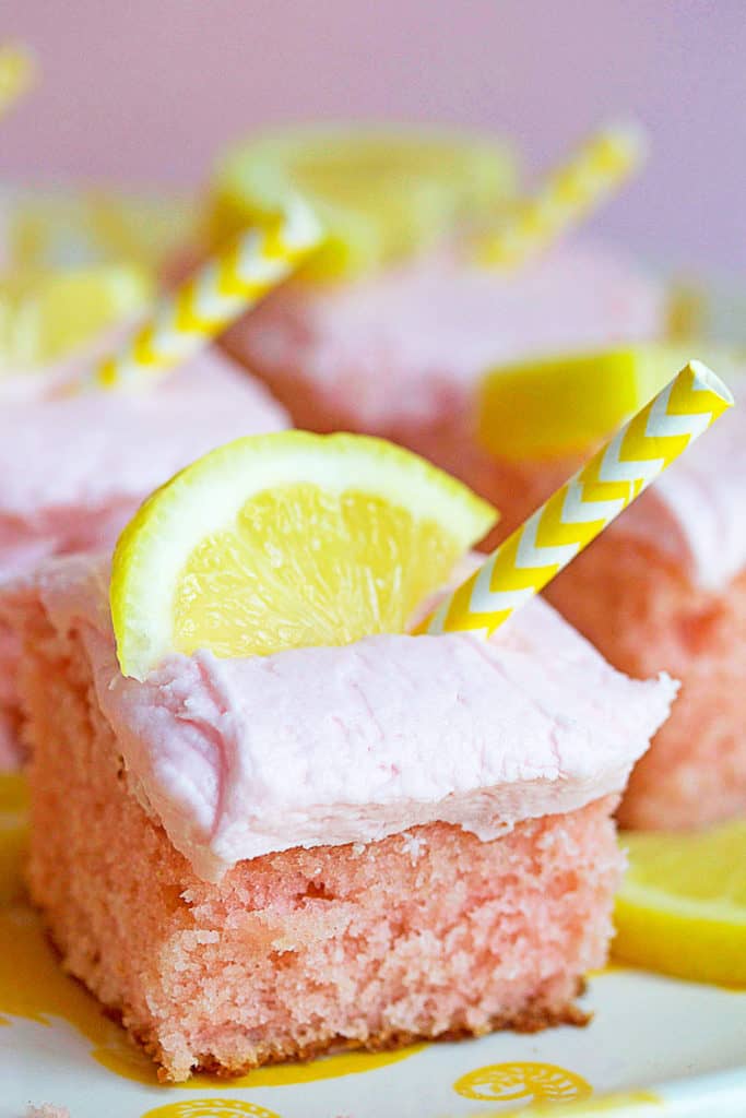 Several slices of pink lemonade cake on a white platter with lemon and yellow straw garnishes