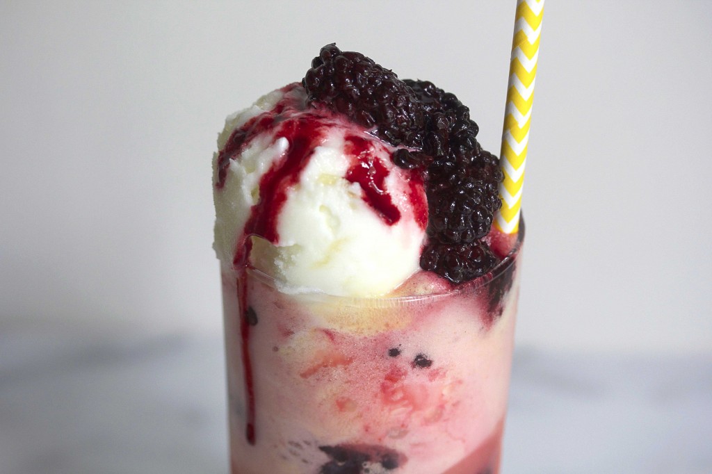 Close up of the top of a blackberry pineapple topped with fresh blackberries and a yellow and white striped straw in it