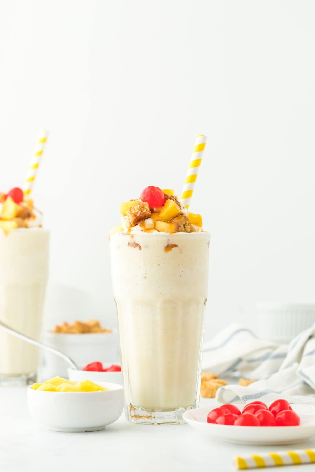 Two glasses of pineapple milkshakes on a table with yellow and white straws.