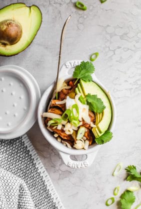 An overhead shot of an individual serving of fajita chili in a small white bowl topped with sliced avocado