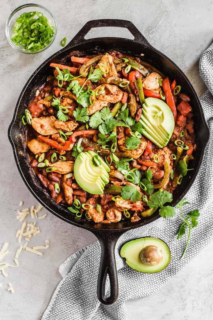 Overhead shot of a black cast iron skillet full of fajita chili with a half avocado and a bowl of cilantro next to it