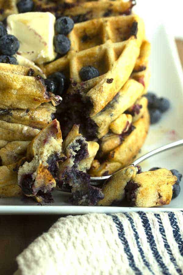 A fork biting into blueberry waffles stack