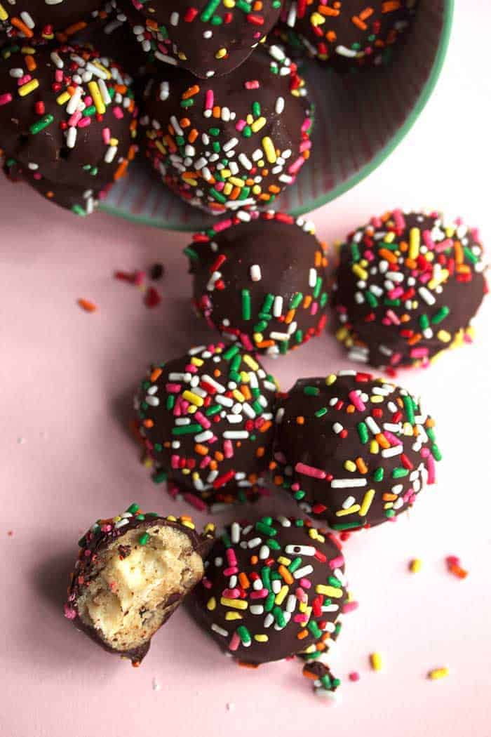 Several cheesecake cookie dough truffles topped with sprinkles being poured out of a green bowl