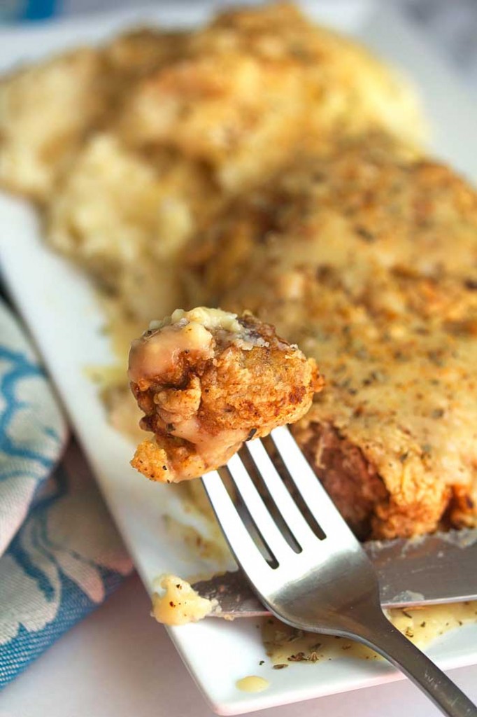 The BEST Chicken Fried Steak recipe piece is on a fork ready to be eaten against a plate of food.