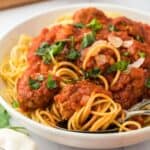 A bowl of spaghetti and meatballs on the table topped with a sprinkle of parmesan and herbs.