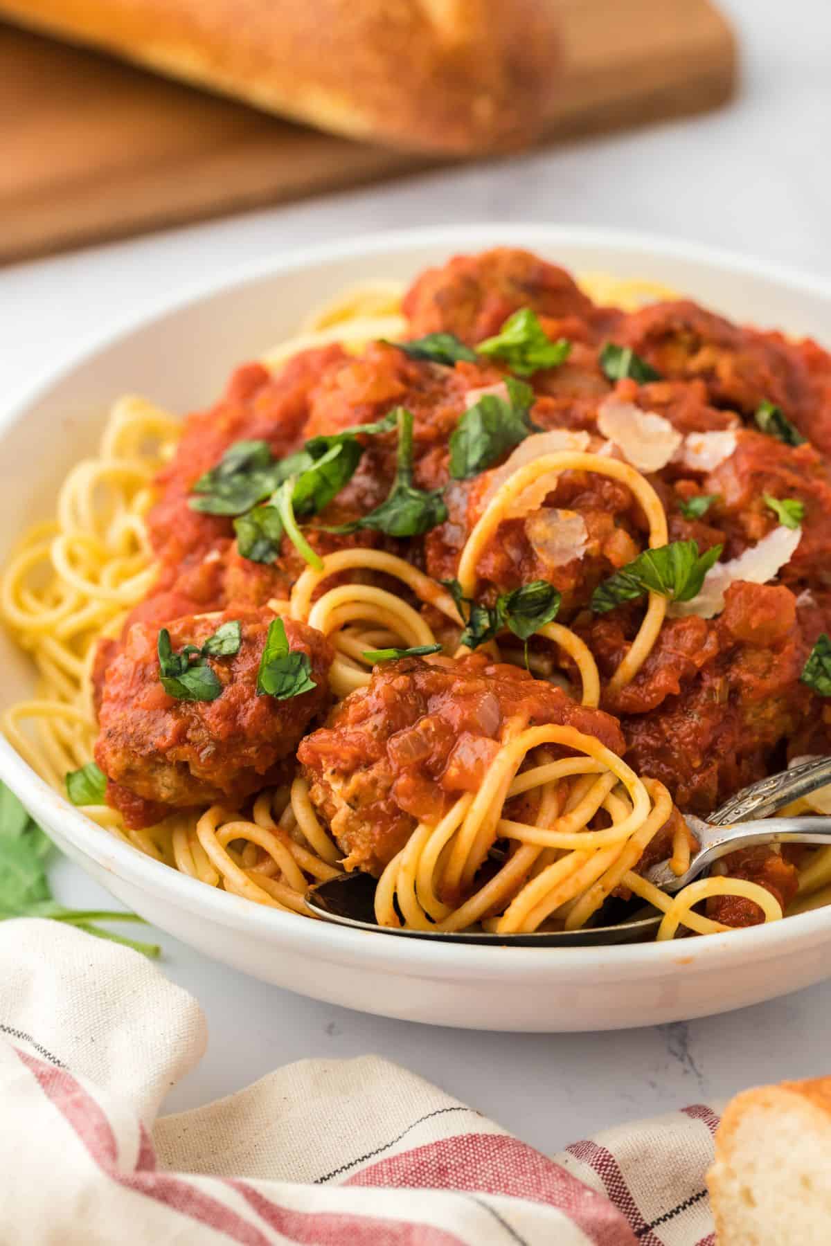A bowl of spaghetti and meatballs on the table topped with a sprinkle of parmesan and herbs.
