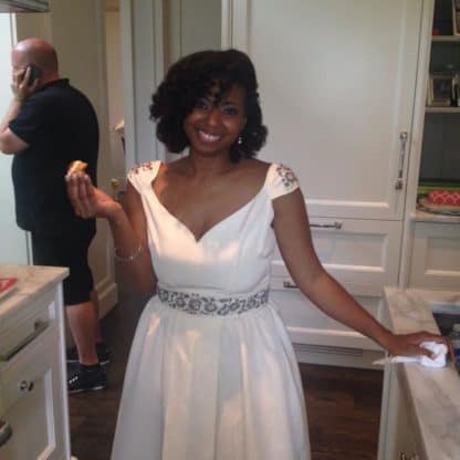 Jocelyn Delk Adams posing in a white, sleeveless dress and holding an appetizer in her right hand