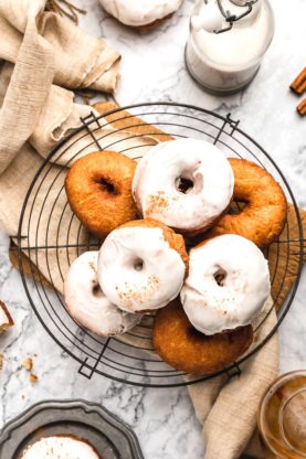 A delicious overhead shot of cider donuts piled high on a round wire rack against a beige napkin