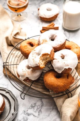 A stack of cider donuts piled high with one glazed and biten into ready to serve against marble background