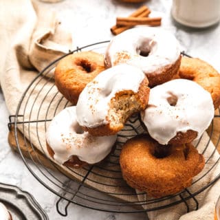 A stack of cider donuts piled high with one glazed and biten into ready to serve against marble background