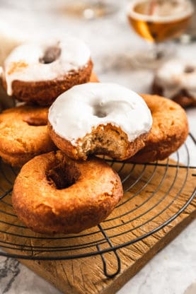 A close up of piled pumpkin donuts with two glazed and the rest plain and one biten into 