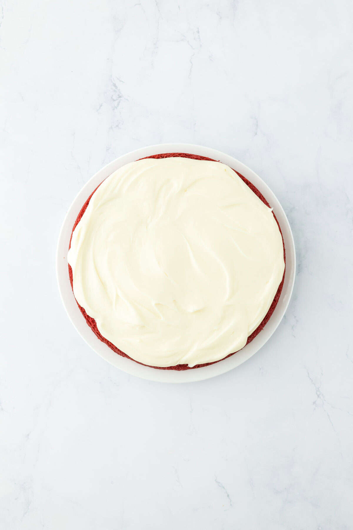 Frosting added to cake layers on white countertop