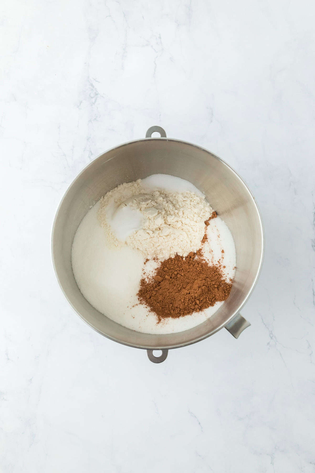 Cocoa, flour, sugar and leavening in a stand mixer bowl on white countertop