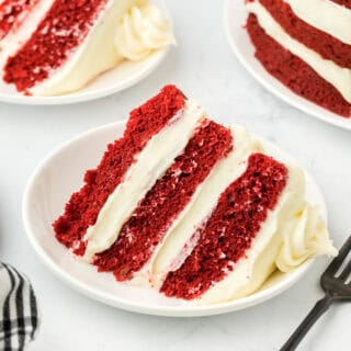 Slices of red velvet cake on white plates with striped black and white napkin