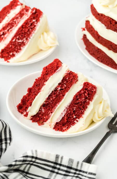 Slices of red velvet cake on white plates with striped black and white napkin