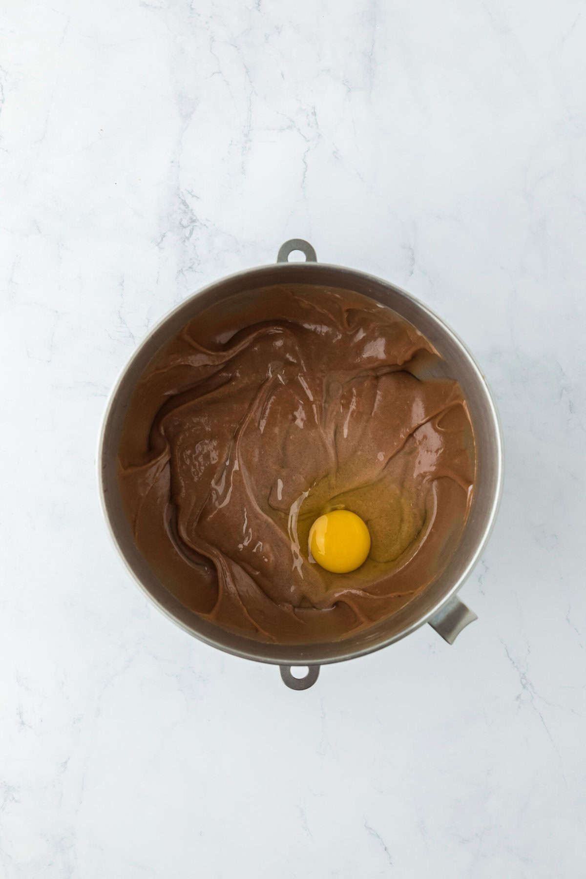 Eggs being added to a chocolate cake batter on white countertop