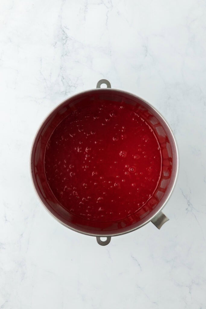 Final red food cake batter in a stand mixer bowl on a white countertop