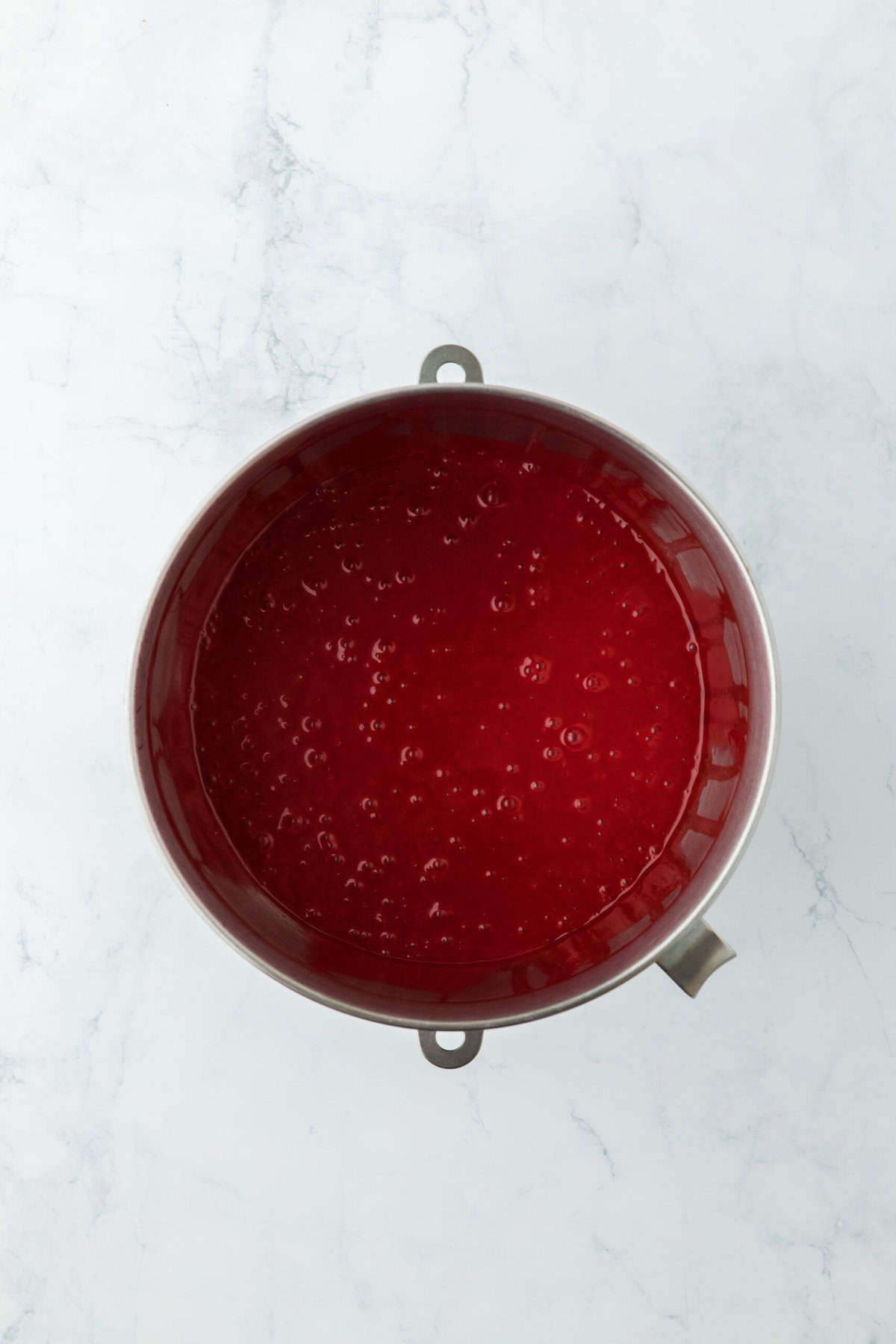 Final red food cake batter in a stand mixer bowl on a white countertop