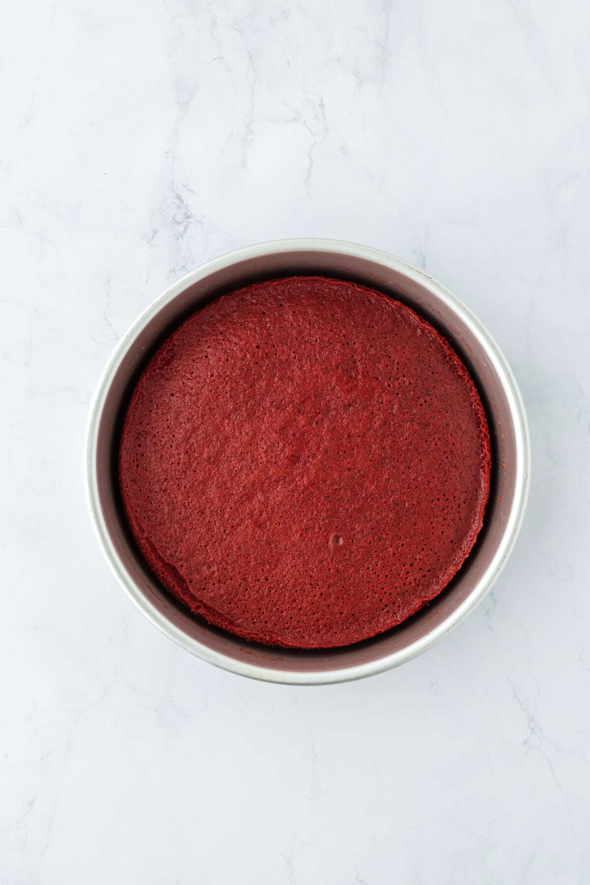 Baked red velvet layer in a prepared pan on white countertop