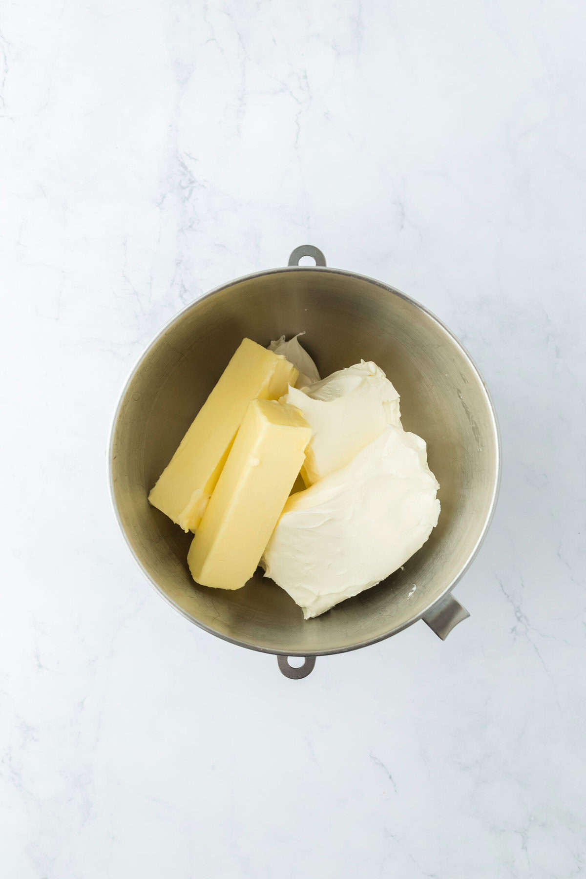 Butter and cream cheese in a stand mixer bowl on white countertop