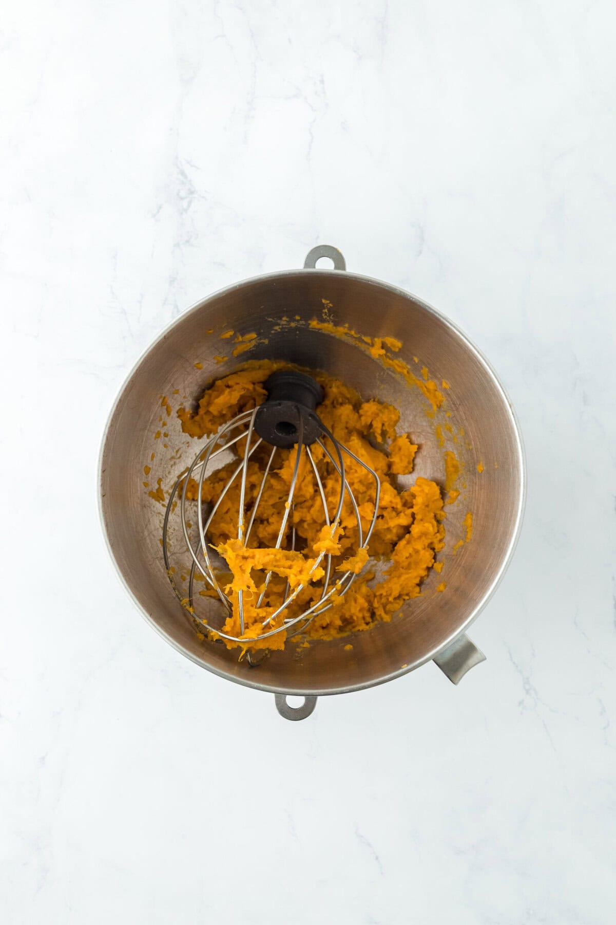 Sweet potato being beaten in a stand mixer bowl removing strings on white countertop