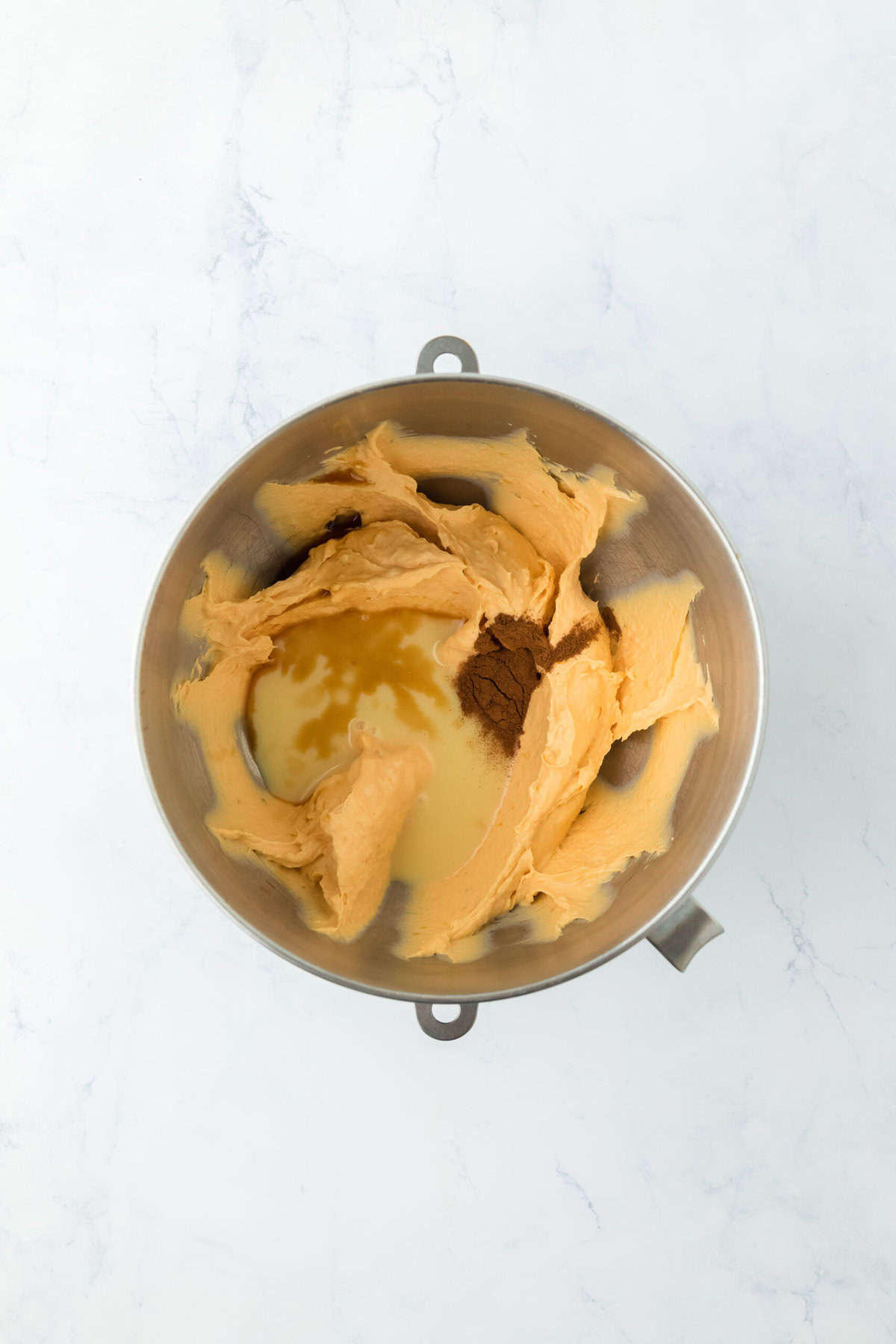 Condensed milk and spices added to stand mixer bowl on white countertop