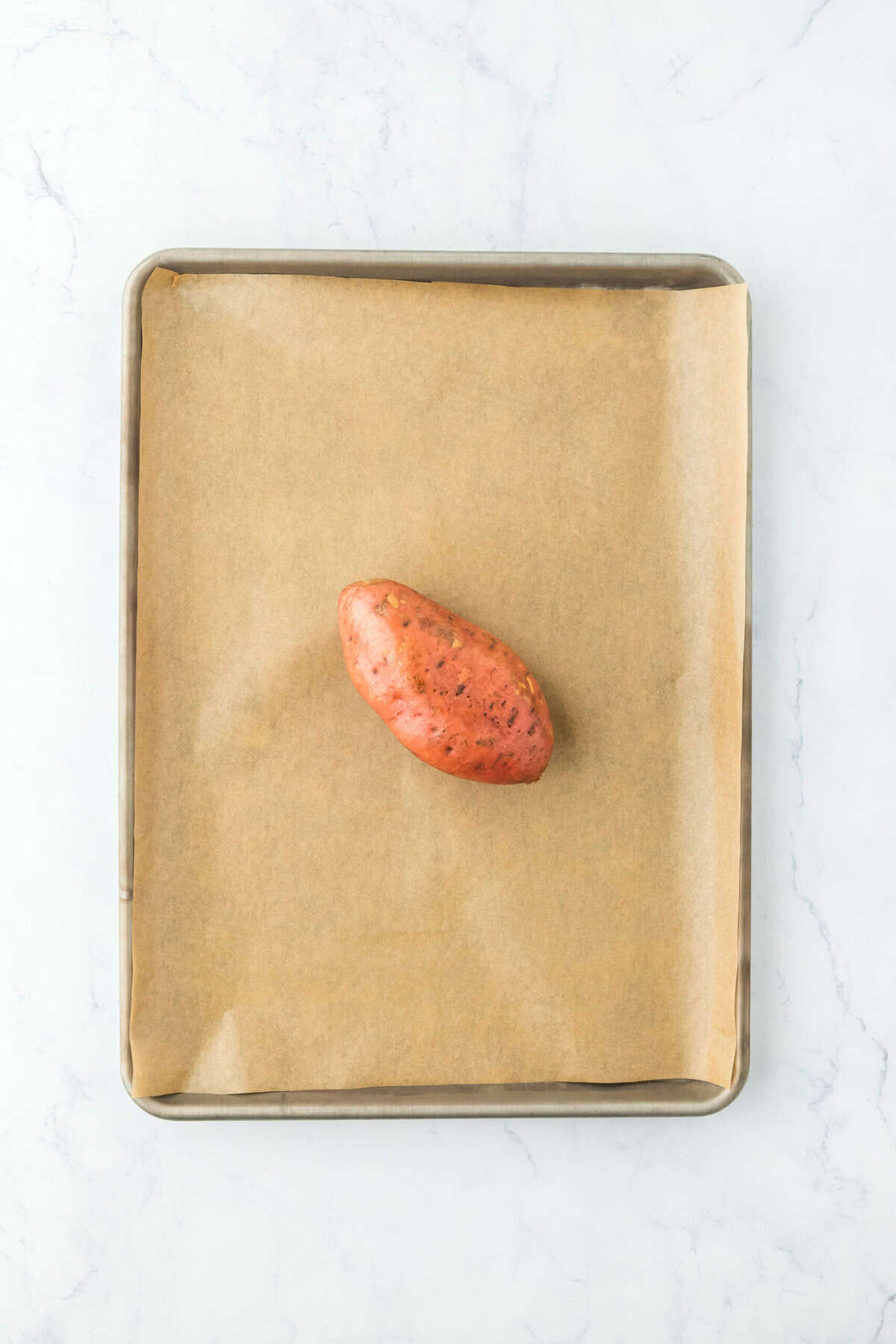 Oiled sweet potato on a parchment lined baking sheet on white countertop