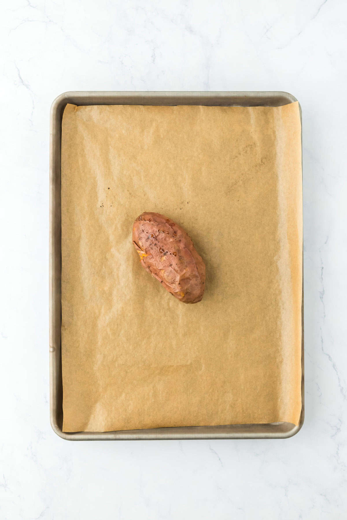 Baked sweet potato on a parchment lined baking sheet