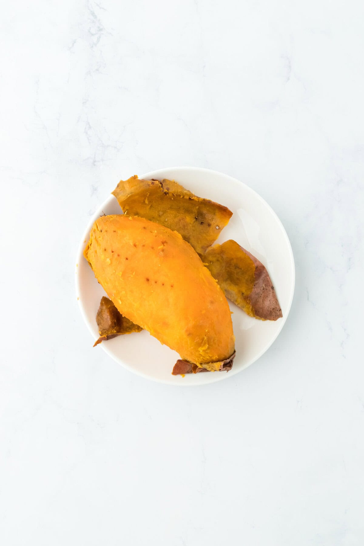 Skin being removed from sweet potato on a white plate on white countertop