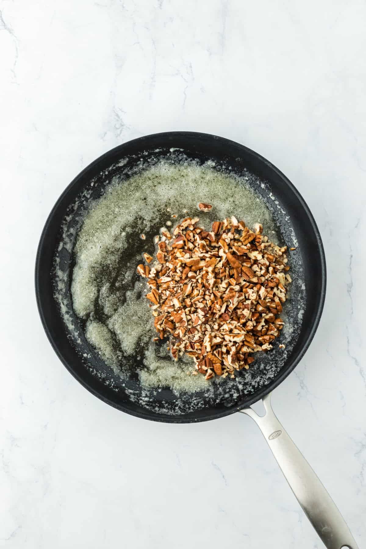 Pecans in melted butter in skillet on white countertop