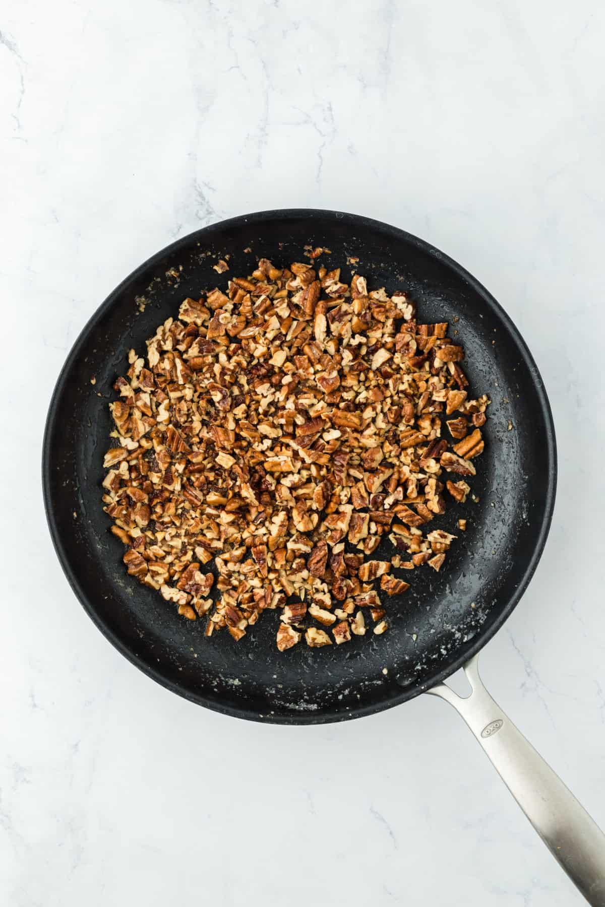 Pecans buttered in skillet on white countertop.