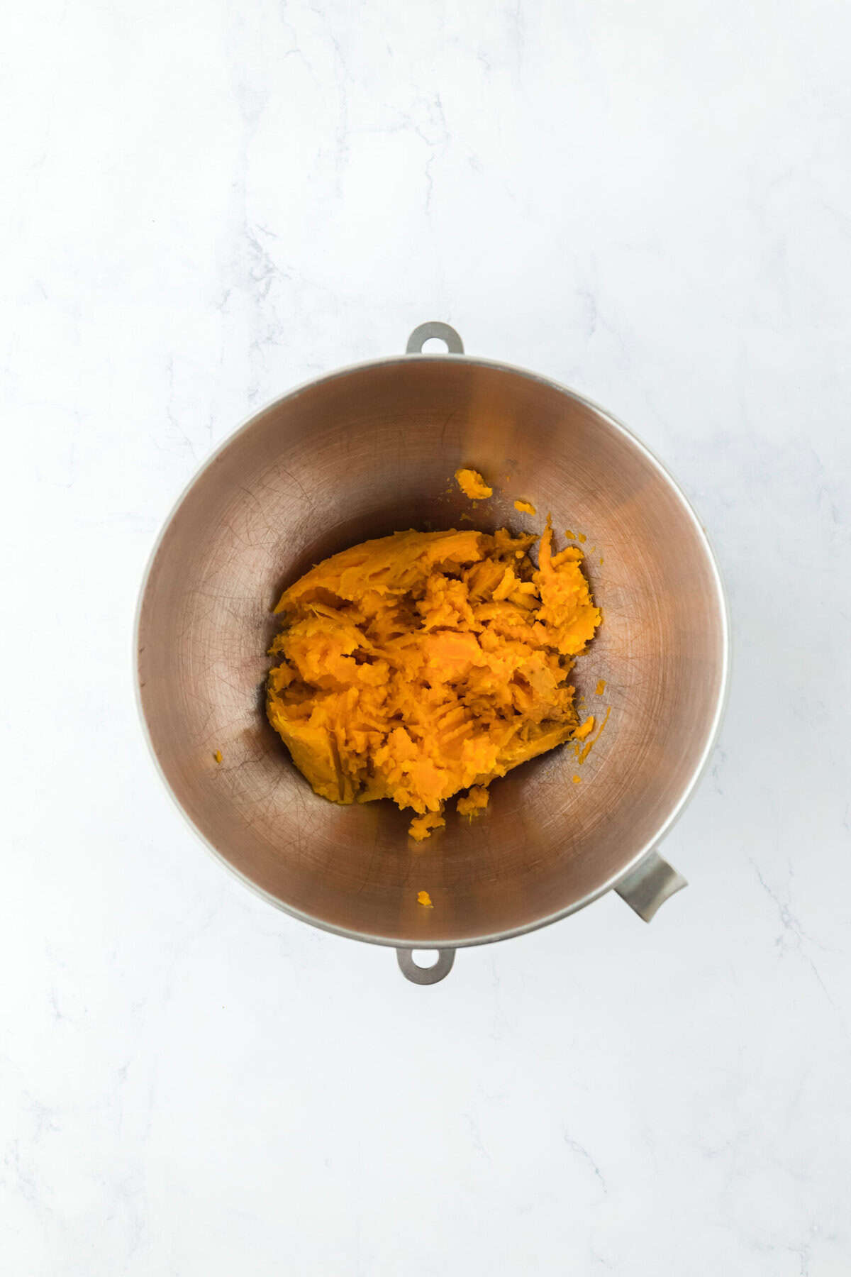 Mashed sweet potato in a stand mixer bowl on white countertop