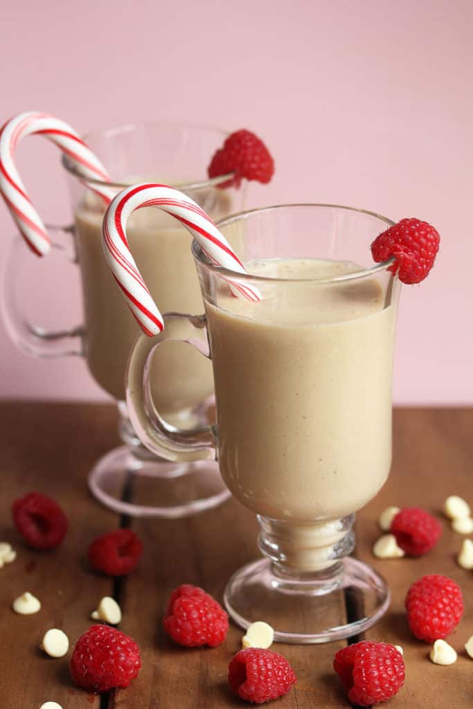 Two glass mugs filled with white chocolate mudslides, a raspberry and a candy cane as a garnish