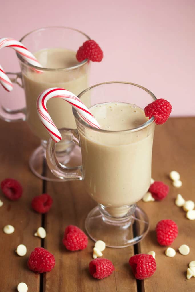 Two glass mugs filled with white chocolate mudslides, a raspberry and a candy cane as a garnish