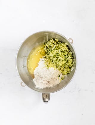 A mixer bowl with zucchini, oil and other ingredients ready to make a zucchini loaf of bread