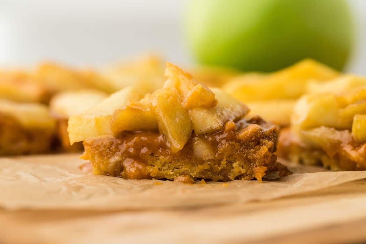 A single caramel apple bar sitting on a wooden cutting board with a green apple in the background.